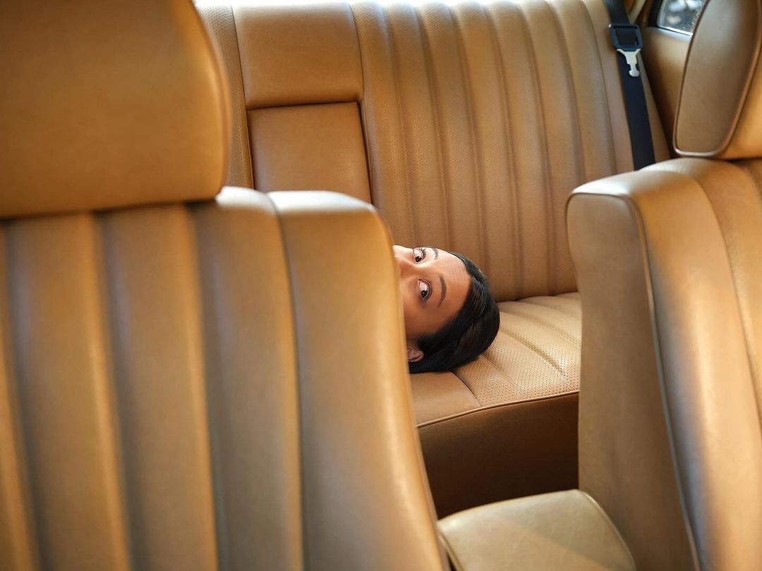 Adult female lies on the tan leather back seat of a car with her eyes open, her dark hair fanned out on the seat.