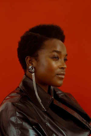 Portrait of a Black woman in a black leather jacket wearing long crystal fringe earrings against a red background.