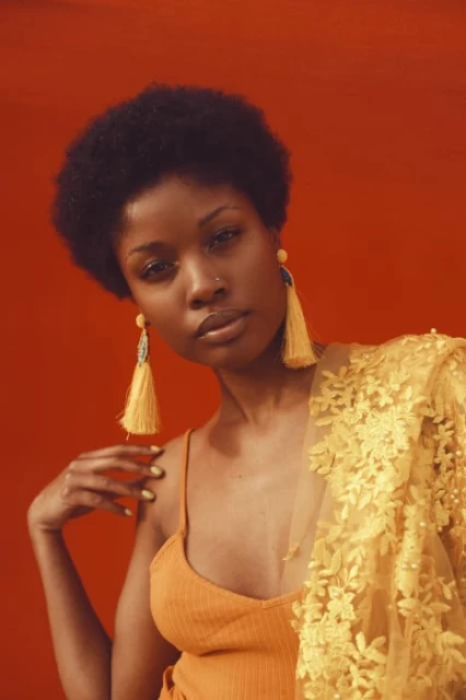 Elegant portrait of an African American woman with an afro, wearing yellow earrings and a sheer floral shawl, against a red backdrop.