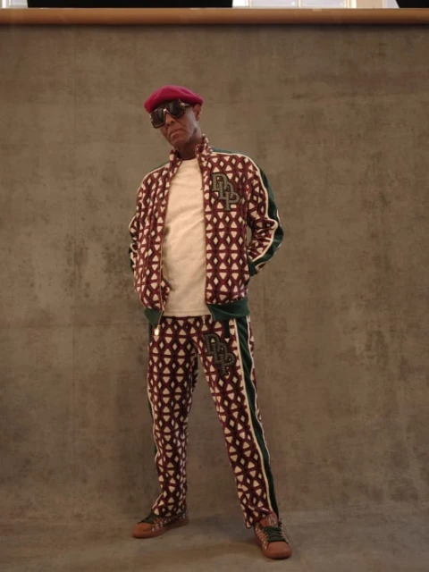 Man in patterned tracksuit and beret poses indoors against a gray backdrop, creating a fashion-forward and stylish portrait. 