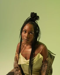 Portrait of a black woman with braided hair wearing a pale top and patterned jacket against a green backdrop
