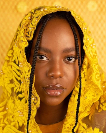 Portrait of a Black woman wearing a bright yellow lace head covering adorned with small white pearls