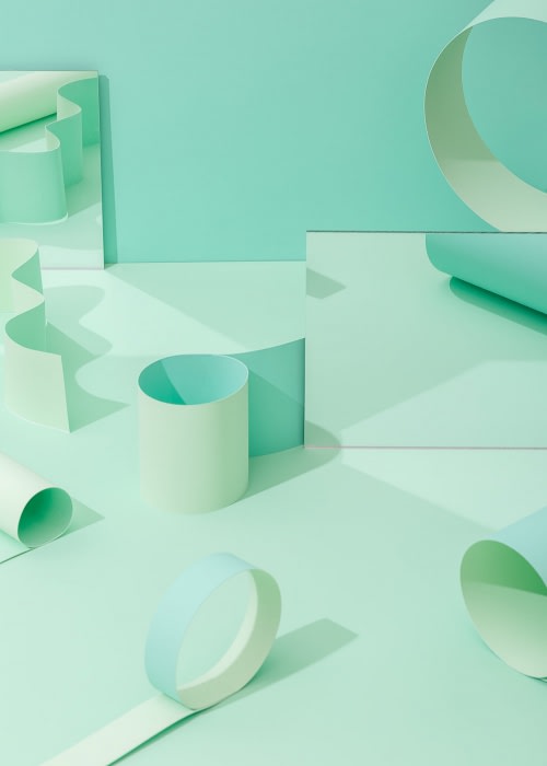 Abstract composition with pastel mint and light green paper cylinders, sheets, and geometric forms arranged in a studio setting.