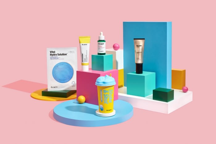 Cosmetic product display featuring bottles, tubes, and a drink cup against a pink background, showcasing various skincare items on platforms.