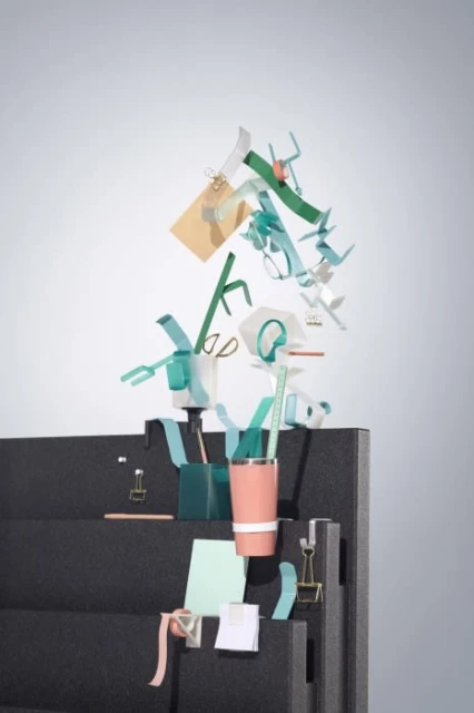 Still life of office supplies: black shelf with clips, pens, pencils, paper, and scissors on a gray background, overhead shot.