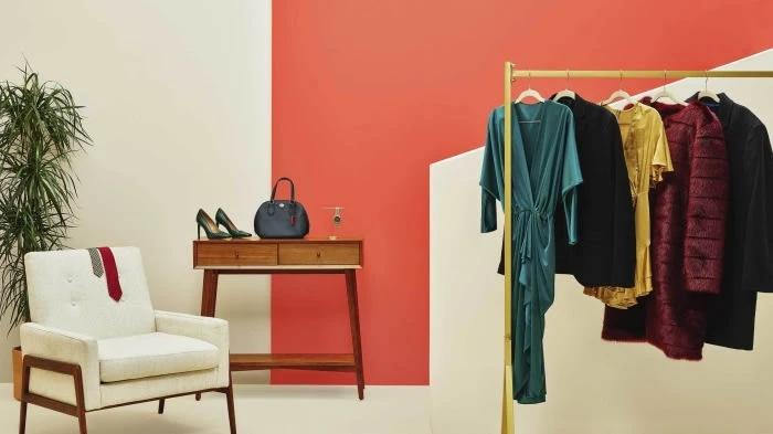 Interior view of stylish clothing rack, chair, table, and accessories, accented by color-blocked wall and potted plant creating an inviting display.