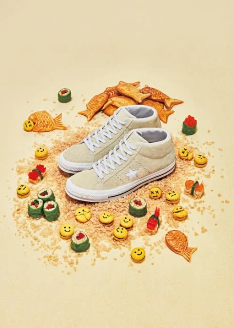 Beige high-top sneakers surrounded by fish-shaped pastries and sushi-shaped macarons on a light beige background in a studio setting.