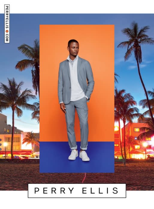 A full shot of a man in a grey suit, posing in front of an orange and blue background with palm trees for a fashion ad.