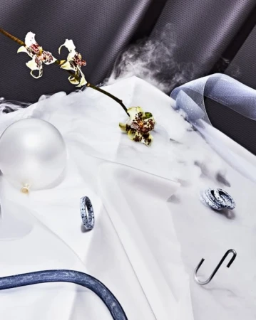 Still life of sparkling rings and a balloon with an orchid, ribbon, and an S-hook on white fabric, backed by textured gray fabric.