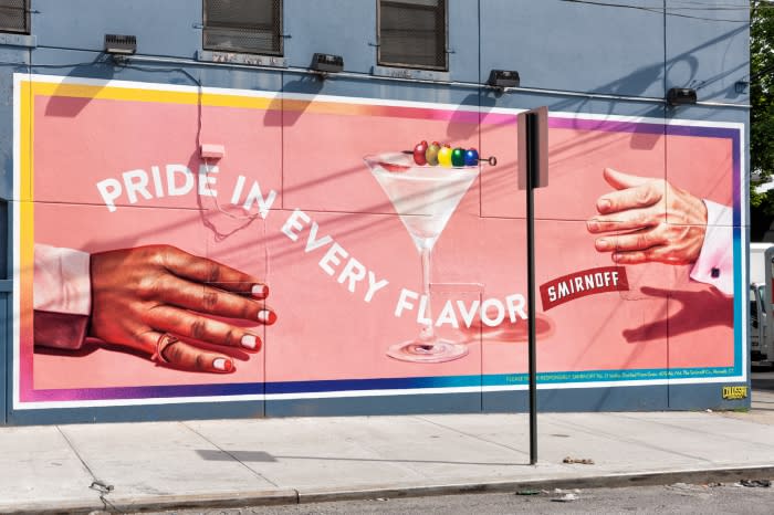A billboard ad with hands holding a martini glass, with a colorful cocktail pick and the Smirnoff logo, against a building backdrop.