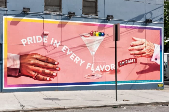 A billboard ad with hands holding a martini glass, with a colorful cocktail pick and the Smirnoff logo, against a building backdrop.