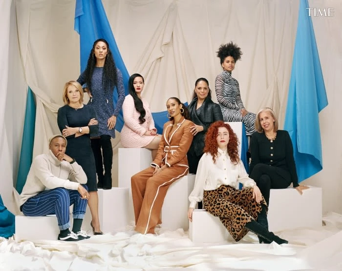 A diverse group of nine women and one man posing on white steps in front of a backdrop for a TIME magazine cover shoot.