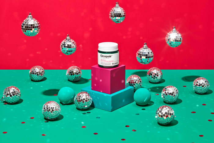 Cicapair skincare product jar sits on pink and teal cubes amid mirrored disco balls and confetti against red and teal backdrop.