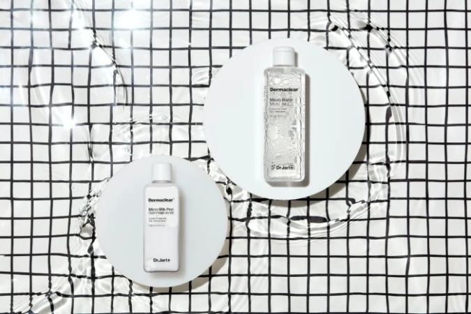 Two bottles of DermaClear skincare product on white circular stands, photographed from above against a black-and-white checkered backdrop.
