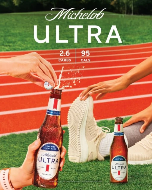 Michelob Ultra beer bottle is opened with splash on running track, with running shoe. Beer advertisement promoting low carb and calorie count.