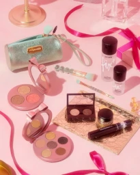 Flat lay of MAC cosmetics and makeup palettes on a pink surface with ribbon