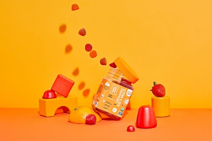 Gummy vitamins and fruits on an orange background. Vitamin bottle is surrounded by colorful candies, strawberries, and citrus fruits.