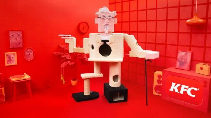 Whimsical, KFC-branded cat tree shaped like Colonel Sanders in a bright red interior studio setting, featuring record player and wall art.
