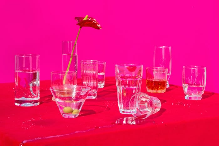 Collection of various glassware and a single red anthurium flower on a bright red tablecloth against a vivid pink backdrop