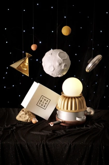 An imaginative still-life composition featuring a robot constructed from kitchenware, positioned on a shimmering black fabric against a starlit backdrop.