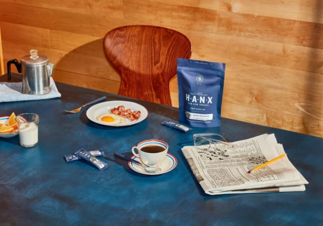 Coffee and breakfast still life: navy table setting with coffee, newspaper, egg, bacon, coffee beans and wood background.