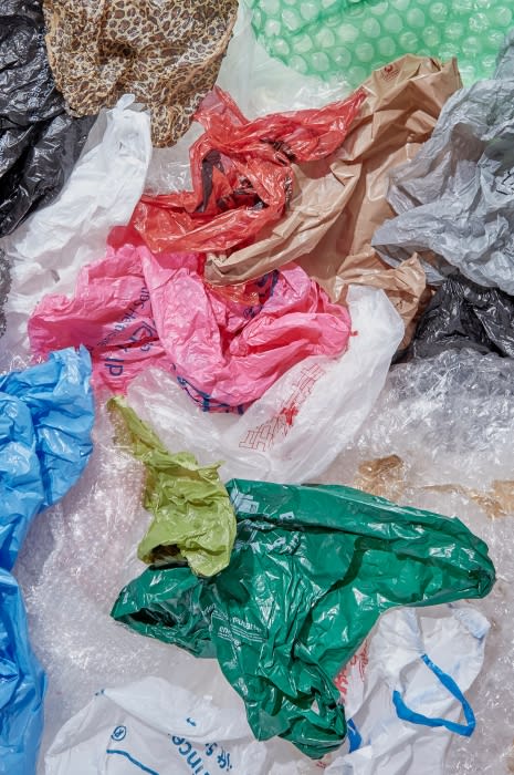 An overhead, close-up shot shows a collection of wrinkled, colorful plastic shopping bags in varying sizes and styles. The heap fills the frame.