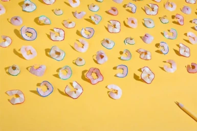Colorful pencil shavings scattered in a neat pattern on a warm yellow background by set designer Liza Nelson