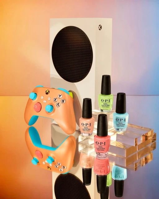 Xbox Series S game console with controller and bottles of OPI nail lacquer in colorful hues, set on a reflective surface.