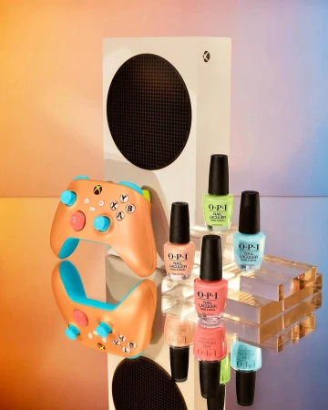 Xbox Series S game console with controller and bottles of OPI nail lacquer in colorful hues, set on a reflective surface.