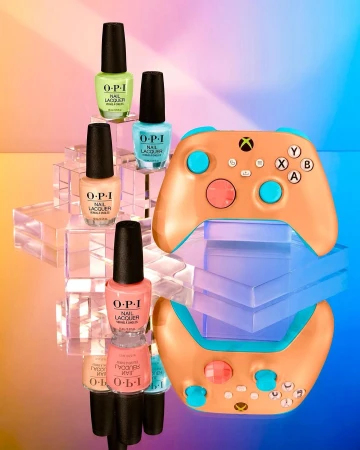 Still life shot of four OPI nail polish bottles on transparent blocks next to a light-brown XBOX controller on a reflective surface.