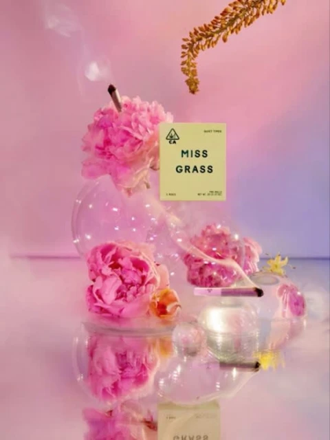 Artistic cannabis product shot with pink peonies, laboratory glassware, and joint with rising smoke, soft pink and blue gradient background.