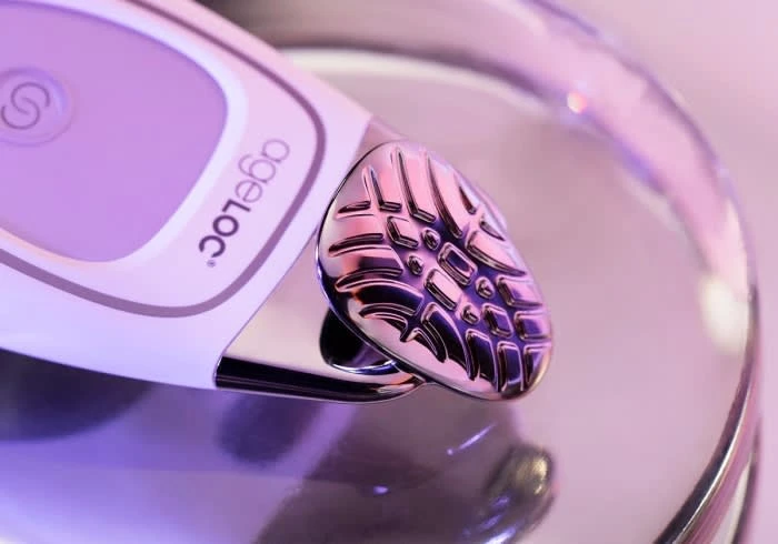 Close-up shot of the ageLOC device with a silver patterned head resting on a reflective surface, lit with purple and white lighting.