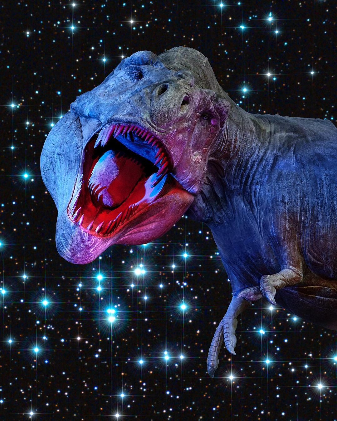Dinosaur Tyrannosaurus Rex with mouth open against background of bright blue and white stars, illuminated with red and blue lighting.