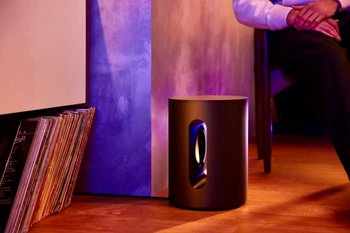 Modern interior with a wireless subwoofer on a wooden floor and record albums against a painted wall with geometric colored lighting.