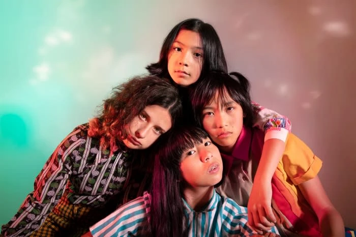 Portrait of four young people in a studio setting with green and red lighting, showcasing their individual styles and expressions.