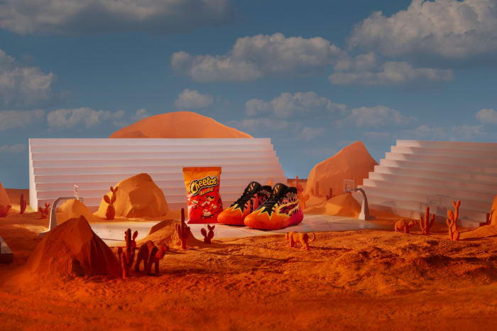 Product shot: Cheetos snack bag and Cheetos-branded sneakers set in a desert landscape with blue sky and white clouds.