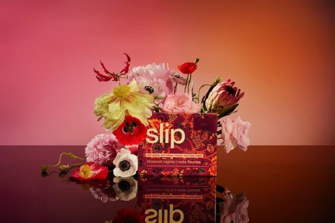 Product shot of a Slip brand box surrounded by flowers in a studio setting with pink and orange gradient lighting.