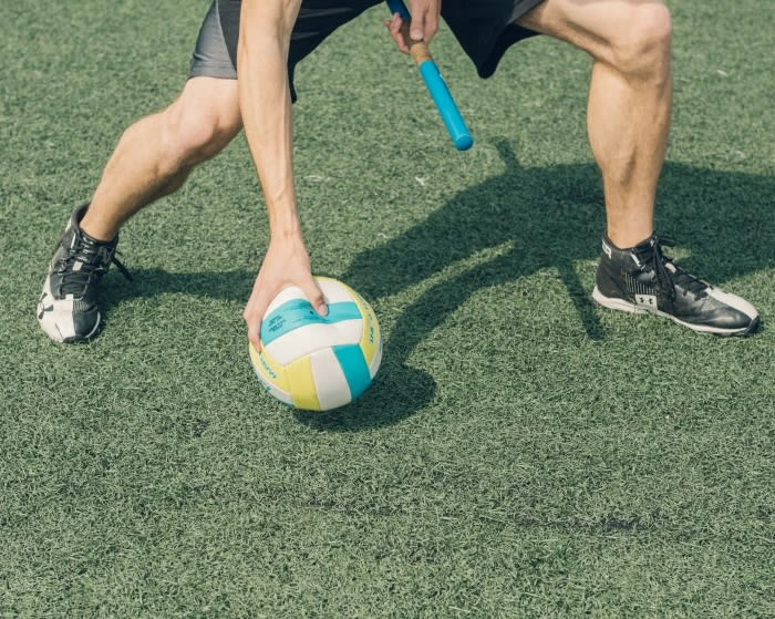 Action shot of a sportsman with a volleyball on a green field, wearing athletic shoes and shorts, and using a blue baton.