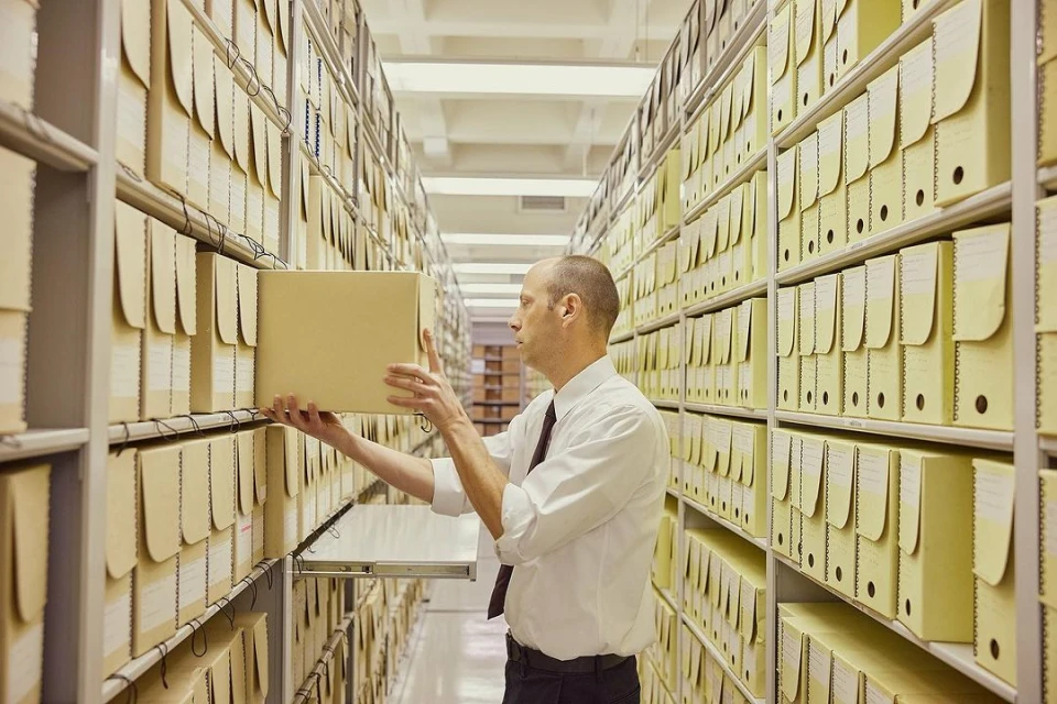 Adult male in a white shirt placing a yellow box on a shelf in a room filled with rows of yellow boxes on metal shelves.