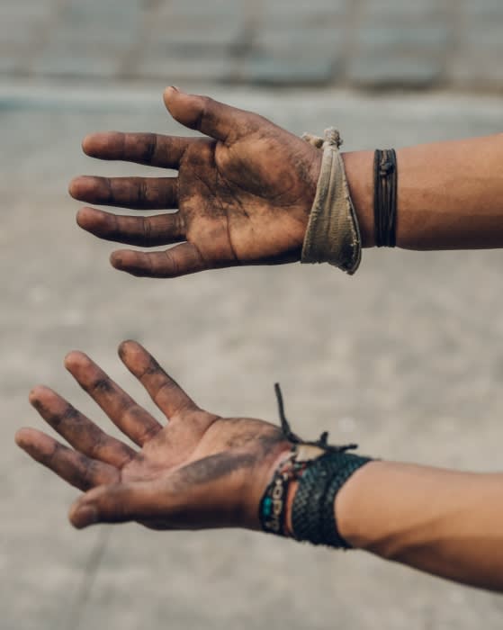 Close-up of two dirty hands outstretched against a blurred background; bracelets adorn the wrists of the arms connected to the hands.