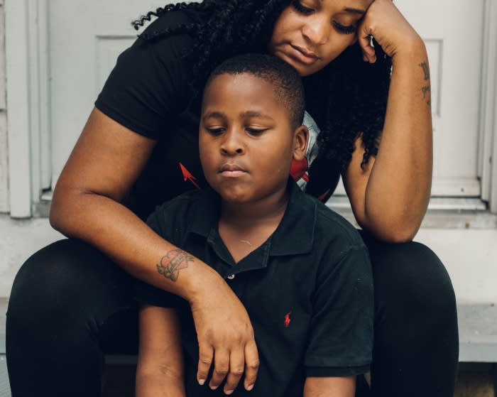 An African-American woman and boy sit on a step, the woman with her head on her hand and the boy looking down with a serious expression.