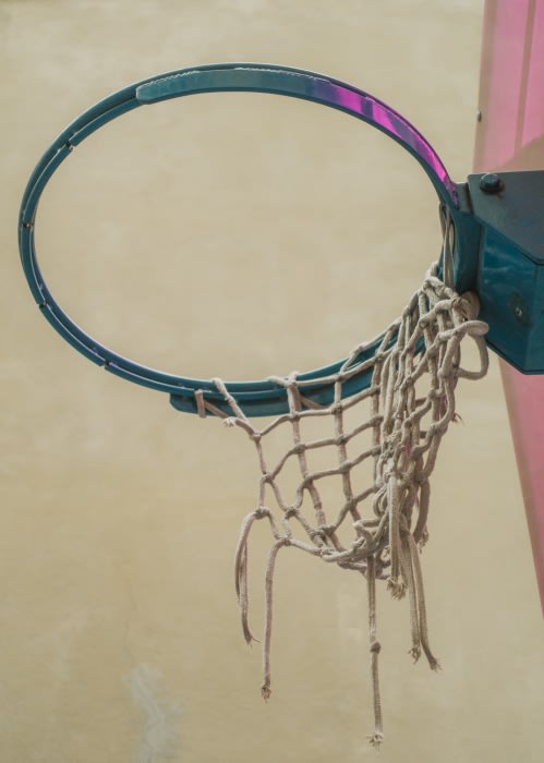 Close-up of a turquoise basketball hoop with a tattered white net attached to it, against a neutral yellow wall.