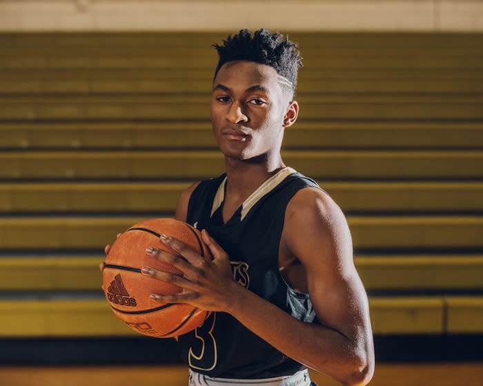 Young man in basketball uniform holding ball indoors. Basketball player looks at the camera with a neutral expression in gymnasium.