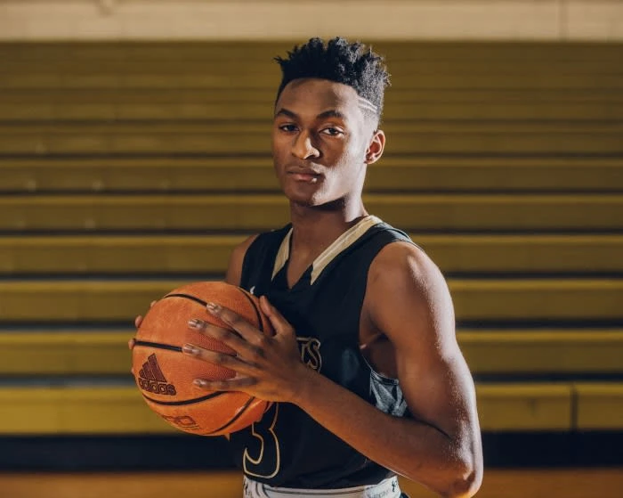 Young man in basketball uniform holding ball indoors. Basketball player looks at the camera with a neutral expression in gymnasium.