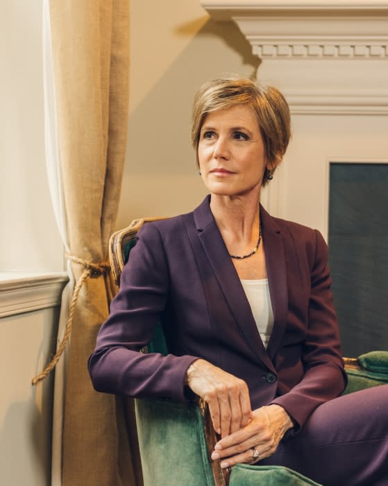 Indoor portrait of a stylish adult woman in a purple business suit sitting in a green armchair, looking away from the camera.