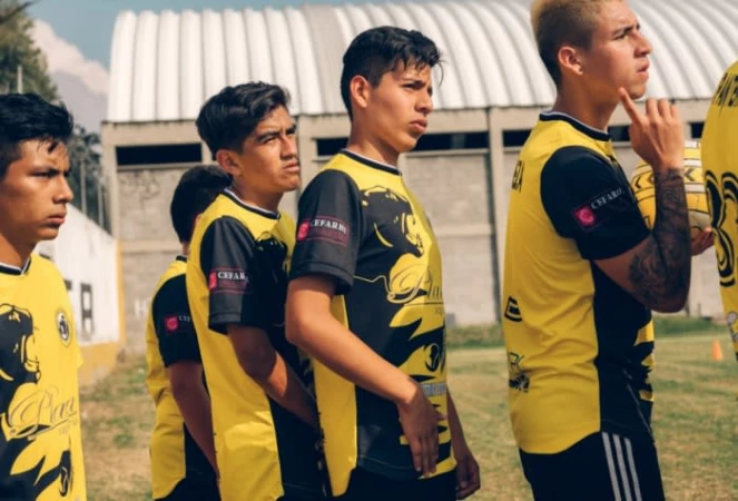 Several young male soccer players in black and yellow uniforms stand on a green grass field, ready to play a game.