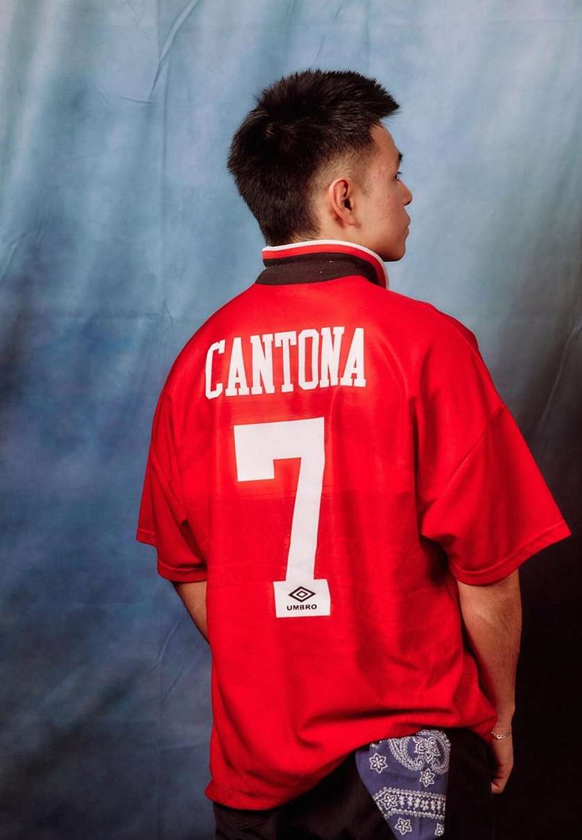 Rear view of adult male wearing a red soccer jersey with white numbering and lettering against a mottled blue and gray background.