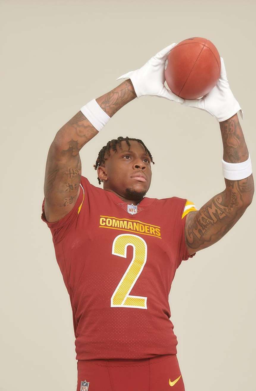 Football player in Commanders uniform, wearing gloves, throwing a football, studio shot on white backdrop. Sports portrait, burgundy and gold.