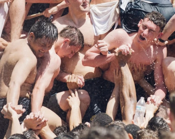 Tight shot of shirtless young men in a dense crowd with arms raised and splashing water, photographed by Jared Soares.