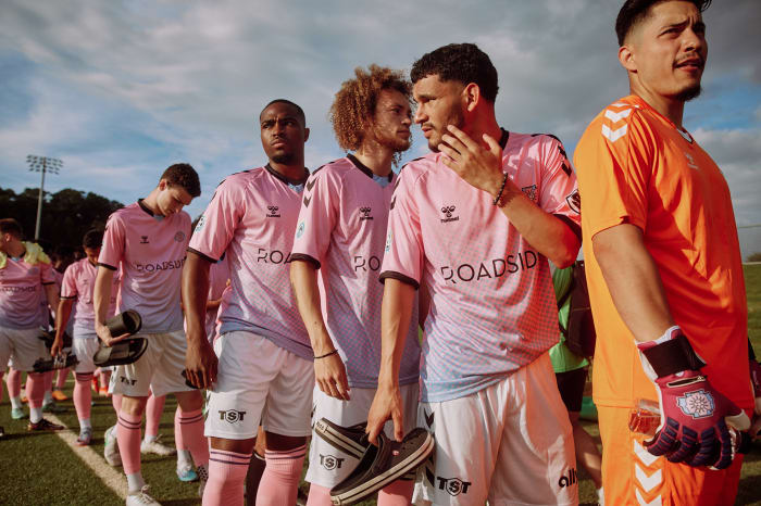 A line of soccer players in pink and white uniforms walking on a field under a bright sky, showcasing team unity and sportsmanship.